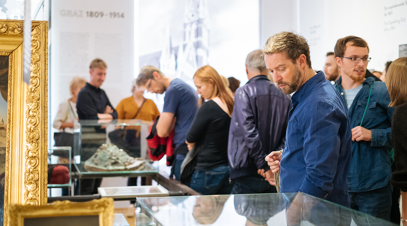 Menschen sind in der Dauerausstellung 360 GRAZ und betrachten die Exponate.