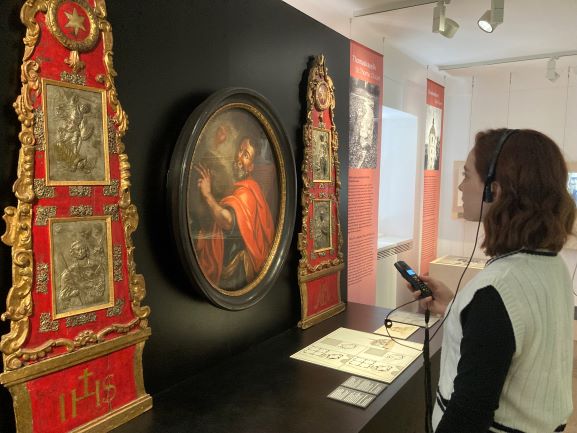 Eine junge Frau betrachtet im Geshcichts-Parcours einen alten Altar, der einst in der Thomaskapelle stand. Sie trägt Kopfhörer.